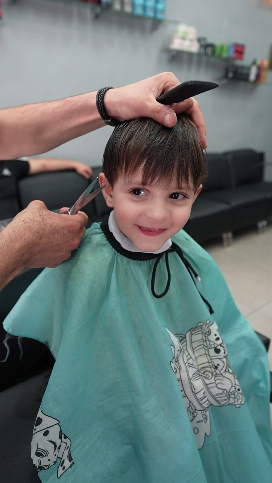 A smiling young boy getting a haircut in a kid-themed cape at Makkawi's